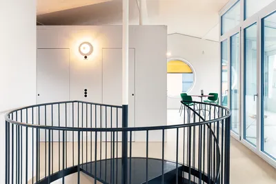 Modernes, frisch gestrichenes Büro in Ferhaltdorf mit schwarzer Wendeltreppe, weißen Wänden, rundem Fenster und stilvoller Beleuchtung – gestaltet vom Malerbetrieb in Winterthur.