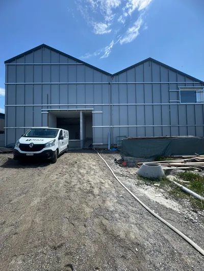 Neu gestrichene Industriehalle in Winterthur mit grauer Metallfassade unter blauem Himmel – professionelle Fassadenarbeiten vom Malerbetrieb in Winterthur.