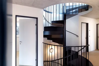 Modernes Treppenhaus in Ferhaltdorf mit eleganter schwarzer Wendeltreppe, weißen Wänden und stilvoller Beleuchtung – professionell gestrichen vom Malerbetrieb in Winterthur.